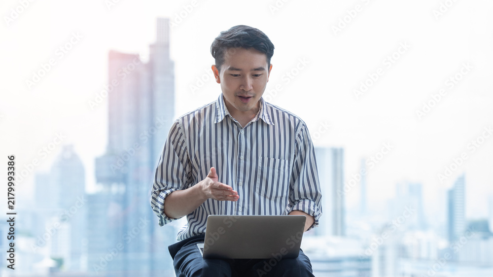 Fototapeta premium Asian Businessman Using Laptop in Modern City Office with Urban Skyline Background