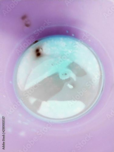 Top view of a purple cup containing a mystery liquid with dark floating particles and light film.