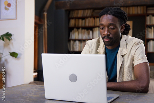 African American man sitting at wooden table working on silver laptop in home study, copy space