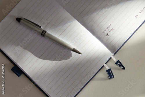 Silver ballpoint pen lying diagonally on lined notebook by window, casting shadow, showing ink note
