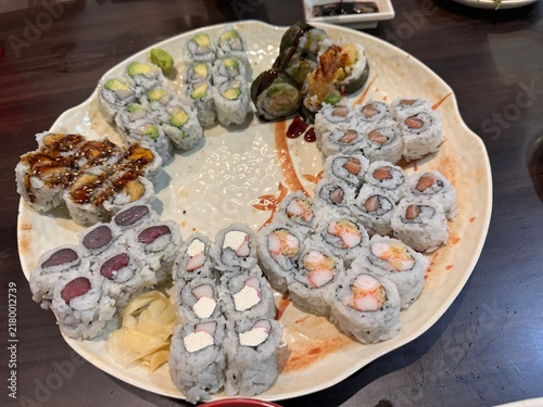 Quadro su tela The image shows a large decorative platter arranged with an assortment of various maki sushi rolls, pickled ginger, and wasabi