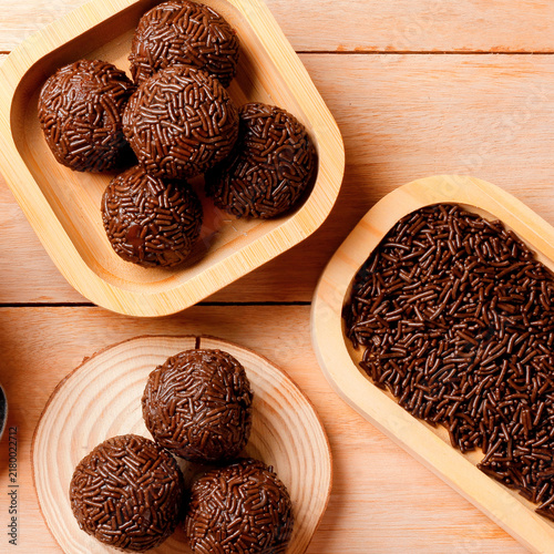 Brazilian chocolate brigadeiro topped with sprinkles, arranged on a rustic bamboo tray on a wooden table.