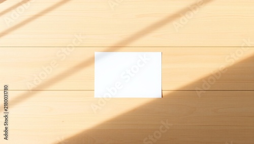 Blank white paper card mockup on a light wooden table with soft sunlight shadows
