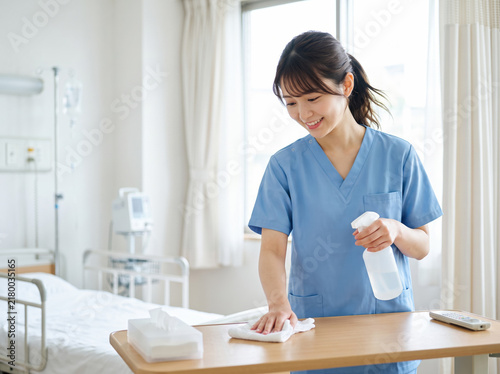 病室のテーブルを消毒して清掃する看護助手の女性