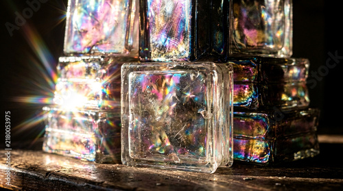 Stack of iridescent glass blocks with light refraction and lens flare on dark background