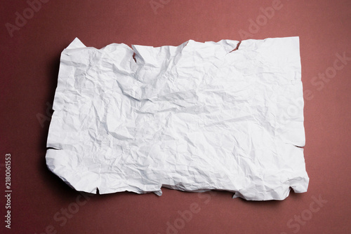 Blank crumpled white paper with torn edges on a dark red background, creating a textured surface with large copy space for text, design, advertising, and creative concepts.