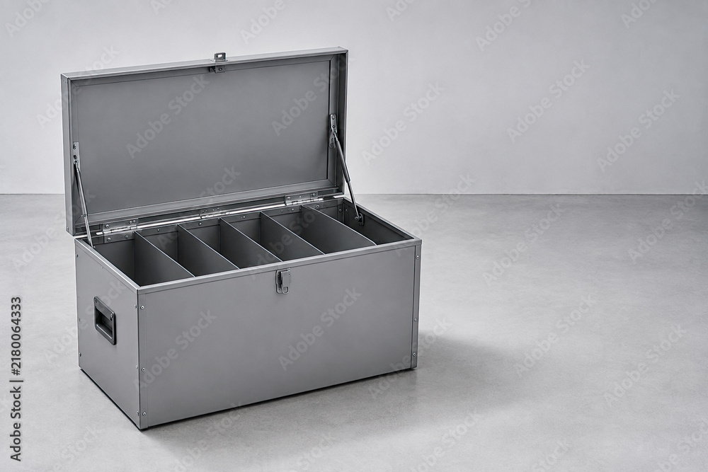 Fototapeta premium Open heavy-duty grey metal storage trunk with internal compartments resting on a concrete floor.