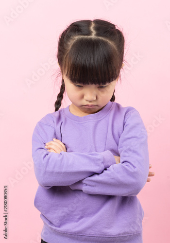 Foto Sulking little girl standing with crossed arms and looking down with a pouty face