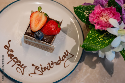 Chocolate birthday cake with fresh strawberries, blueberries, and flowers on a plate.