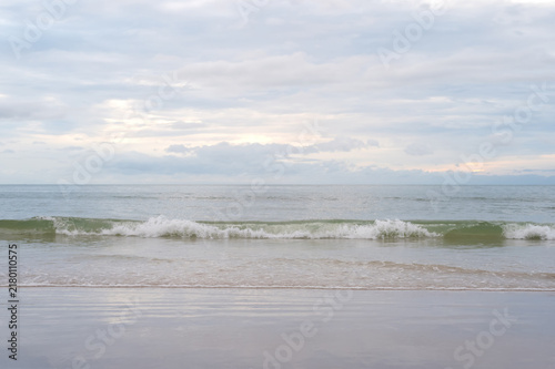 Gentle waves rolling onto a sandy beach under a cloudy sky.