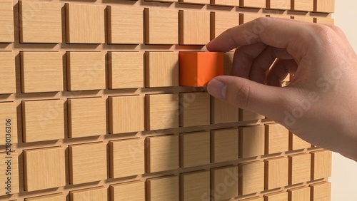 Hand placing small orange block into wooden grid toy on brick wall background