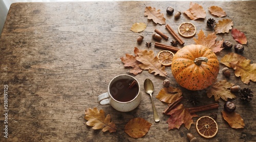 Flat lay composition of colorful autumn leaves, a single pumpkin, cinnamon sticks, and a warm cup of coffee on a stone surface, with copy space.