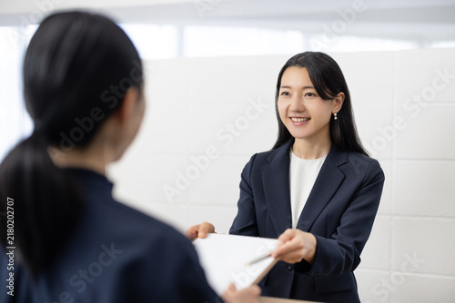 Young Japanese woman in a suit handing documents to a client