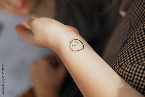 Close-up of a small hand-drawn henna face motif on a person’s wrist, featuring a simple smiling expression and rounded outline in warm natural light