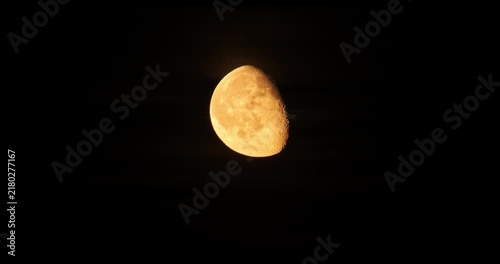 Time lapse of a glowing yellow gibbous moon moving slowly across a pitch black night sky background