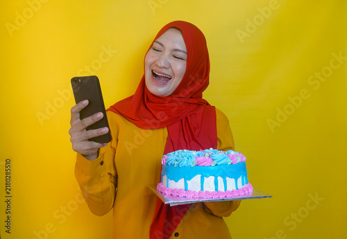 Young Asian Muslim Woman Doing Video Call On Phone While Holding An Icing Cake