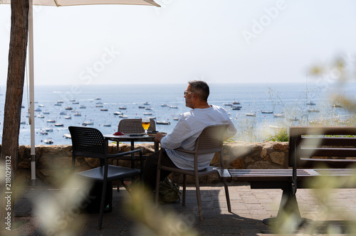 Fotografía Man sitting at a table with a glass of beer, looking out at the Mediterranean Se