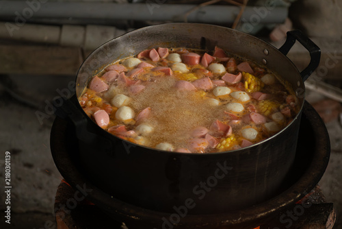 Quadro su tela Close-up of hot soup with sausages, corn and fish balls simmering in a large pot