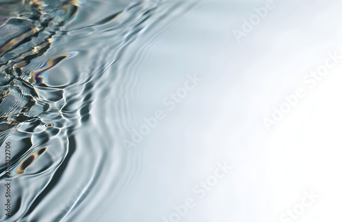 a thin layer of iridescent oil naturally floating across clear water, creating delicate swirling bands of muted cyan, violet, amber and green with generous clean negative space for advertising copy