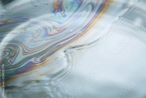 a thin layer of iridescent oil naturally floating across clear water, creating delicate swirling bands of muted cyan, violet, amber and green with generous clean negative space for advertising copy