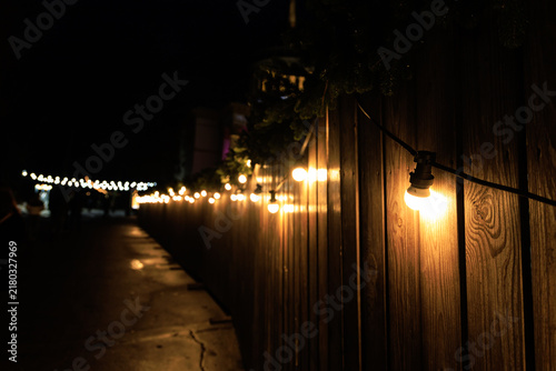 Fotografía String lights glow along a wooden fence in a nighttime setting with additional l