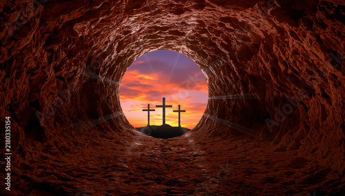 View from inside a tomb looking out at three crosses against a dramatic sunset sky