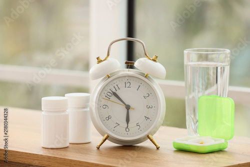 Quadro su tela Alarm clock with pills and glass of water on shelf in room, closeup