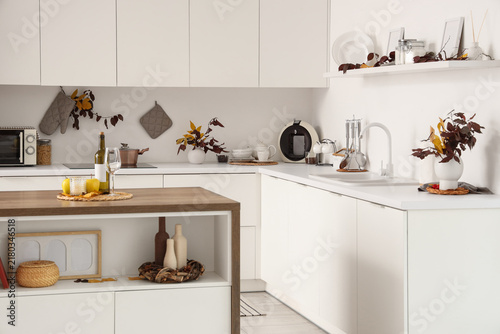 Interior of modern kitchen with autumn leaves, table and counters