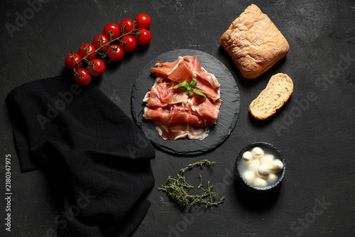 Fotografía Board with delicious prosciutto slices, ciabatta, cherry tomatoes and bowl of mo