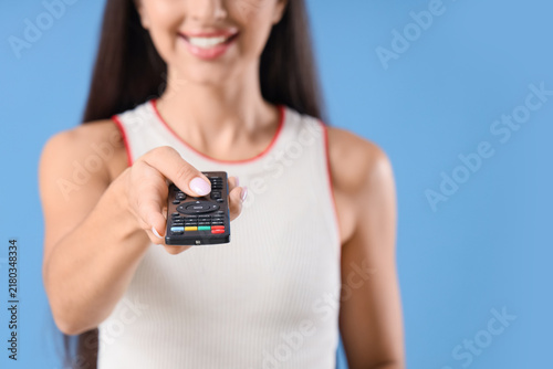 Pretty young woman with remote controller watching TV on blue background, clo...