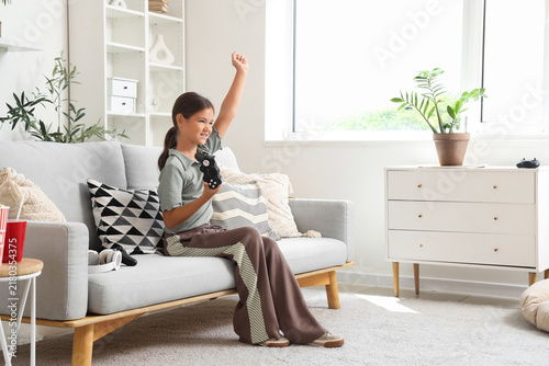 Happy little girl playing video game on sofa at home