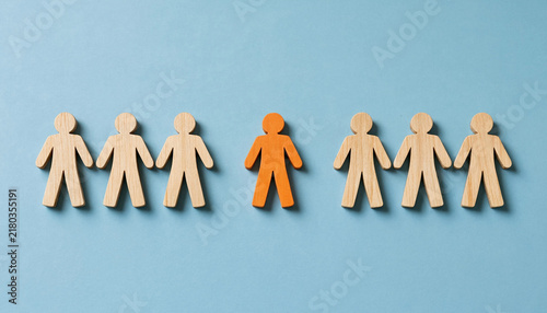 Wooden figurines in line with one orange figure standing out representing individuality concept on blue background