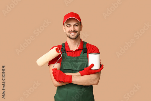 Fotografie Portrait of male painter with roller and can of paint on beige background