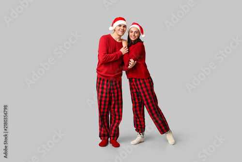 Happy young couple in Christmas pajamas and Santa hats on grey background