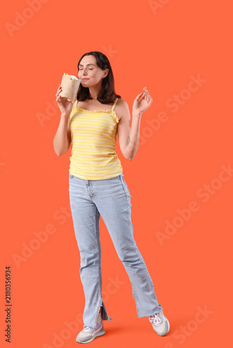Beautiful young woman with french fries on orange background