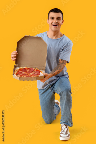 Young man with tasty pepperoni pizza on yellow background