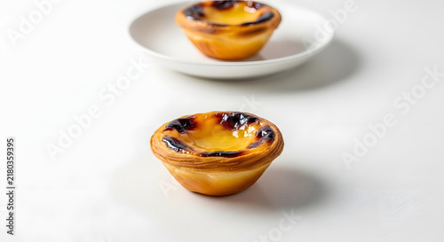 Pastel de Nata Delights: Two delicious Portuguese custard tarts, with their signature caramelized tops and flaky pastry, are presented on a minimalist white background, ready to be savored.