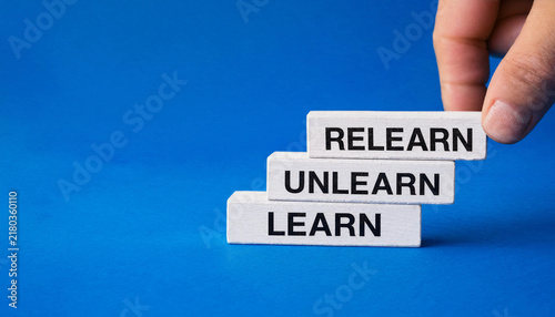 Hand placing wooden block with relearn text on top of unlearn and learn blocks against blue background symbolizing continuous learning concept