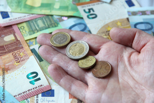 A close-up of a hand holding cents on a background of cash euros symbolizing money, savings, wealth, financial success, investments, and economic prosperity, with a table full of cash.