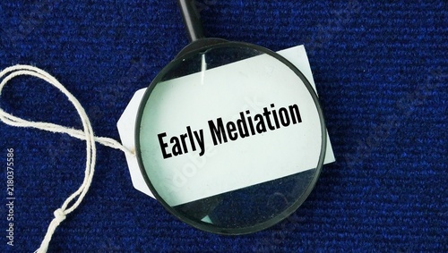 Magnifying glass and paper tag with the words Early Mediation. a voluntary or court-ordered process in which disputing parties meet with a neutral third-party mediator to resolve a conflict before inv