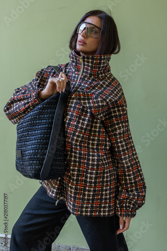 Casual urban outfit with fashionable woman combining plaid oversized jacket, wide black trousers, sneakers and statement handbag for modern street style