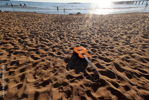 People on the beach and a guitar on the sand.