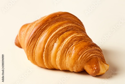 Fresh croissant laying on a flat beige surface viewed from an angle