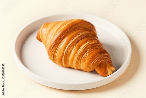 Fresh croissant laying on a beige plate viewed from an angle. Beige background