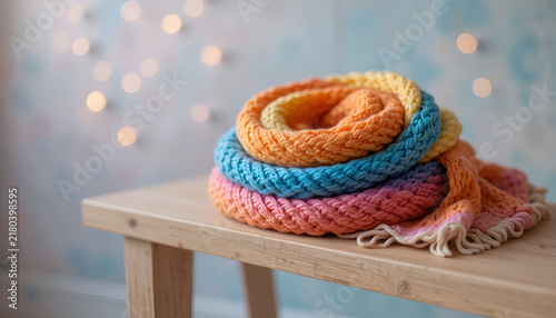 Colorful crochet rainbow scarf folded on a wooden bench with cheerful lifestyle background
