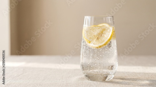 Premium sparkling water in a clear glass with floating lemon slices, condensation droplets, soft natural sunlight
