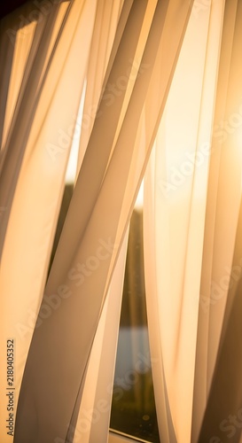 Soft white curtains hanging in front of a window with warm golden hour sunlight shining through