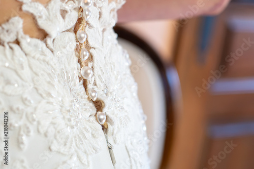 Close up detail of the back of a white wedding dress with pearl buttons, zipper and delicate floral lace embroidery with beads and sequins, elegant bridal gown craftsmanship on wedding day morning