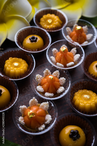 Traditional golden Thai sweets are placed on a wooden table, adorned with banana leaves and flowers