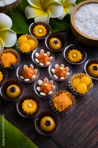 Traditional golden Thai sweets are placed on a wooden table, adorned with banana leaves and flowers